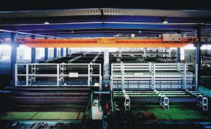 as Materialhandling übernimmt eine Lasttraverse mit patentierten Greiferarmen, die je nach Ausführung bis zu drei Lagen der Stapeljoche gleichzeitig transportiert und umstapelt.